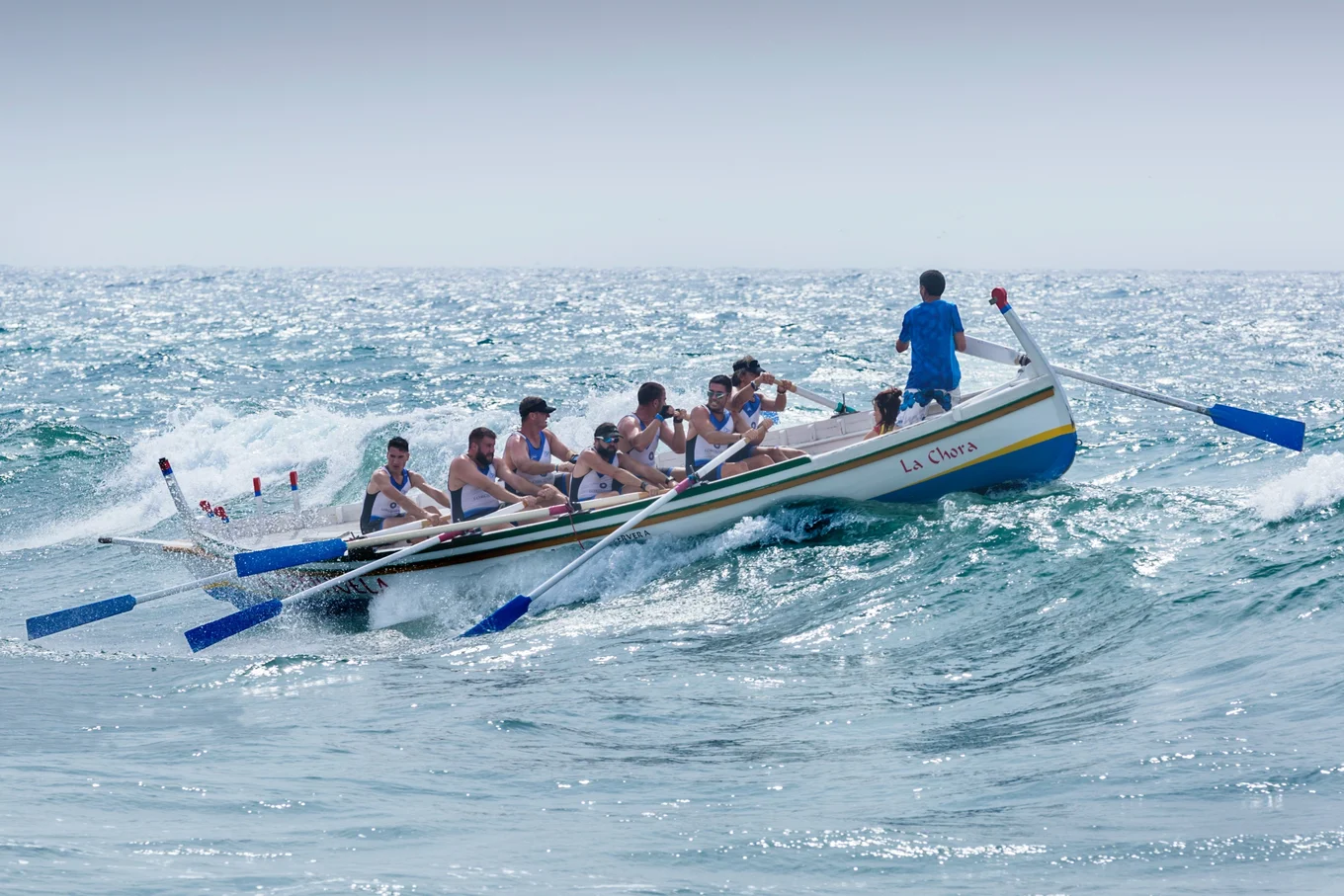 Boat with eight rowers on a wavy sea.